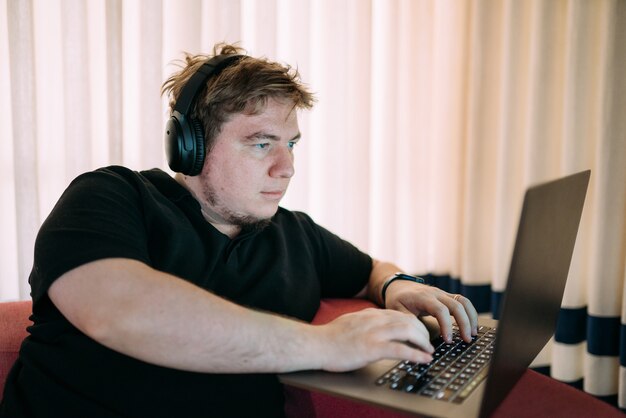 Concentrated man sitting at home using laptop computer, with headphones