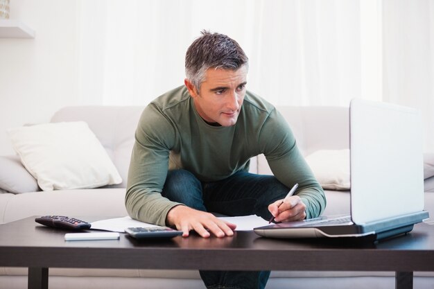 Concentrated man using laptop and taking notes 