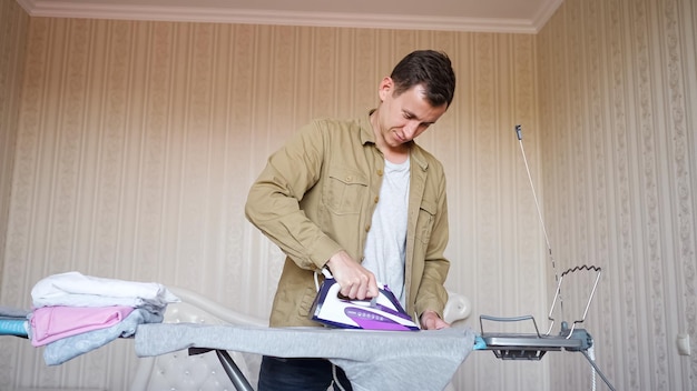 Concentrated man wearing brown shirt does chores and irons