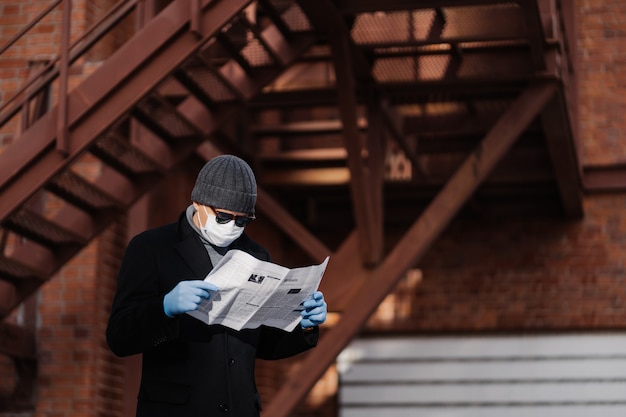 Concentrated man wears sunglasses and coat, medical mask