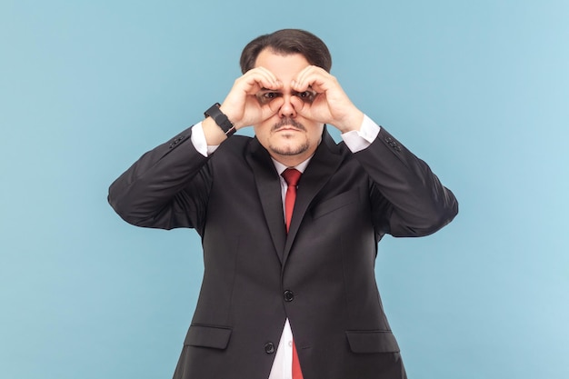 Concentrated man with mustache standing and looking at camera through binocular making with hands