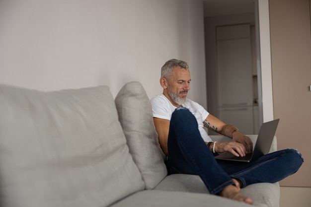 Uomo concentrato che lavora al suo laptop su un divano