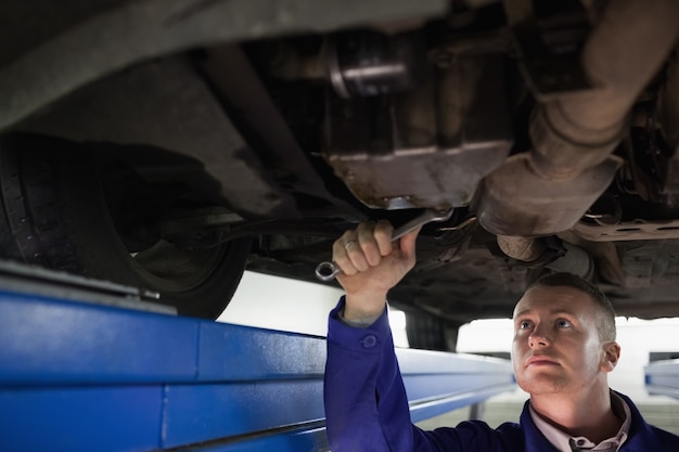 Concentrated mechanic repairing the below of a car