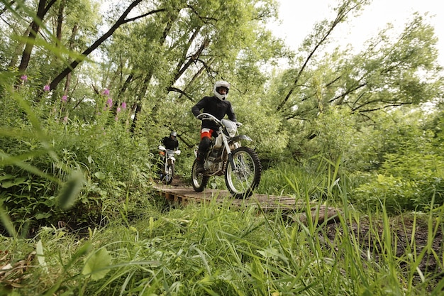 Concentrated motorcyclists in protective wear crossing fragile wooden bridge while participating in motorbike competition