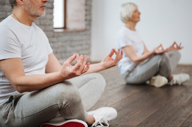 Concentrated people sitting on the floor crossing their legs putting arms on knees while being in yoga poses