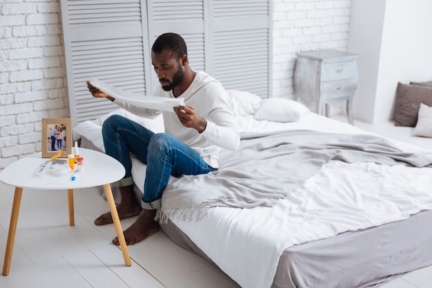 Concentrated person. Serious calm young man looking very concentrated while sitting on a bed with a white towel in hands