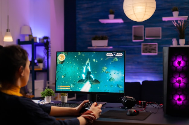 Concentrated player sitting on gaming desk late at night using\
wireless controller playing space shooter. virtual streaming cyber\
performing live tournament using professional equipment