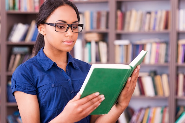 Concentrated on reading. confident african female student reading a book while standing in library