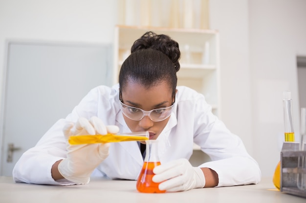 Concentrated scientist pouring orange fluid 