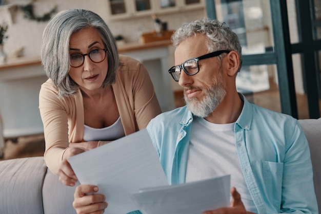 Concentrated senior couple in casual clothing taking care of their finances while bonding together at home