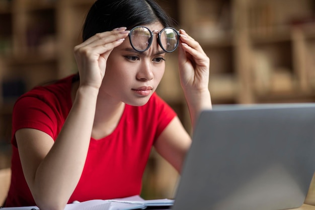 La studentessa coreana adolescente intelligente concentrata si toglie gli occhiali guarda la lezione online nel laptop