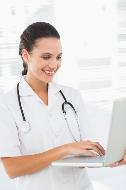 Концентрированный улыбается женщина-врач, используя ноутбук