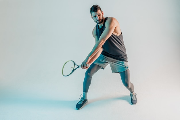 Concentrated sportsman hold racquet and play tennis. Young bearded european tennis player. Isolated on turquoise background. Studio shoot. Copy space