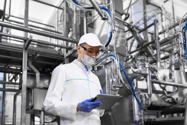 Concentrated technologist taking necessary notes with help of digital tablet while standing at production department of dairy factory inspector carries out control at the cheese factory