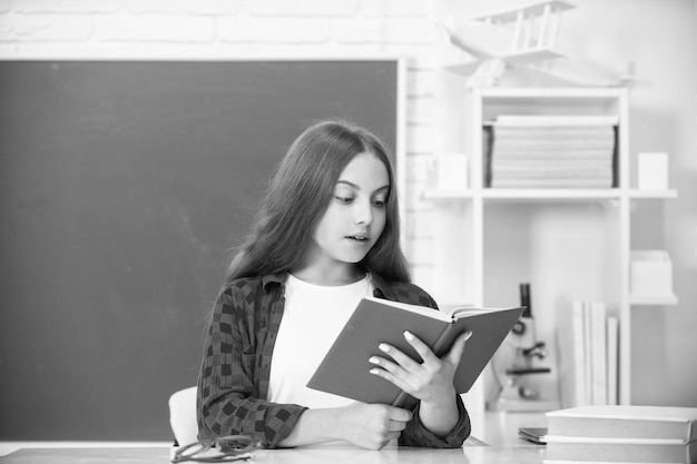 Concentrated teen girl in high school read workbook at blackboard knowledge