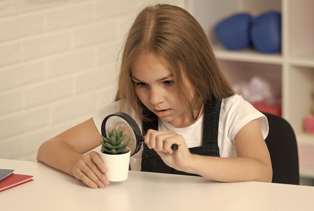 Concentrated teen girl looking at plant through magnifying glass knowledge