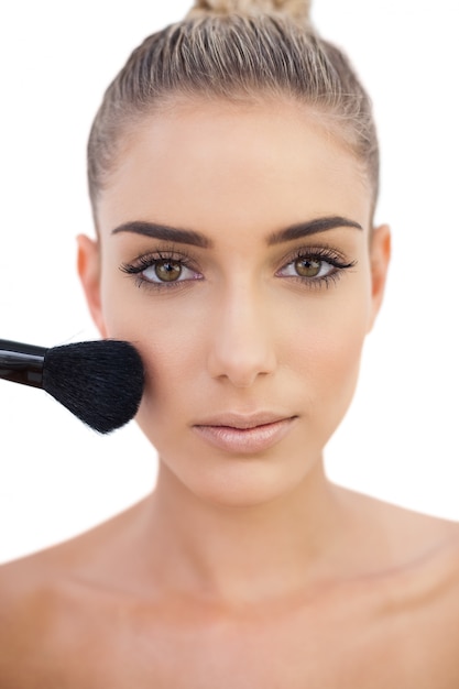 Concentrated woman applying powder on her cheeks