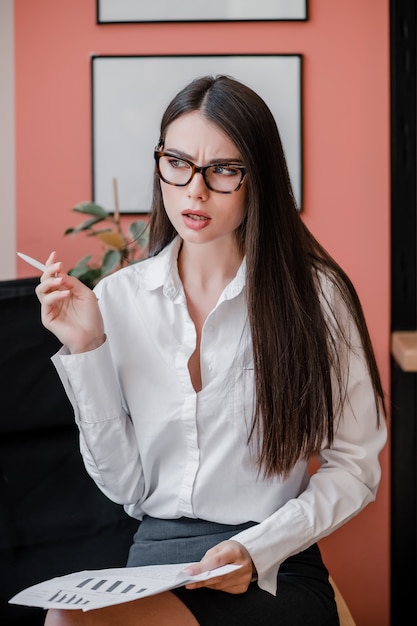 Concentrated woman in glasses thinking with papers in her hands