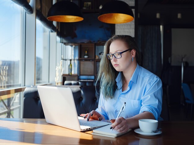 Concentrated at work. Confident young woman plus size in smart casual clothes working on laptop while sitting near window in creative cafe