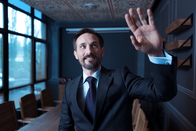 Foto concentrato sul lavoro. uomo attraente premuroso bello alzando la mano e guardando lo schermo virtuale mentre si lavora con dispositivi tecnologici moderni
