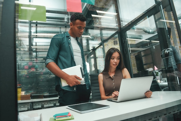 Concentrato sul lavoro giovane donna asiatica e uomo afroamericano in abbigliamento casual guardando