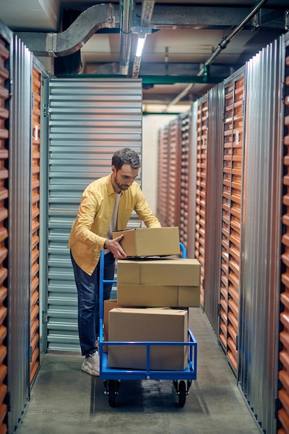 Photo concentrated worker stacking boxed goods on the platform trolley