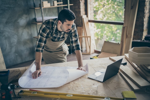 Concentrated workman stand near table have white construction plan look in computer watch building workshop in house home garage