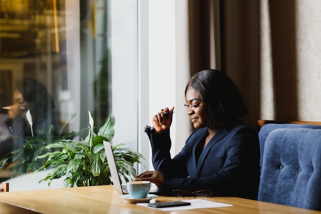 Photo concentrated young african women working on laptop while sitting at working place