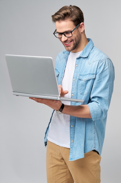 Сосредоточенный молодой бородатый мужчина в очках, одетый в джинсовую рубашку, с помощью ноутбука