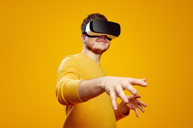 Concentrated young bearded man wearing virtual reality helmet touching the air