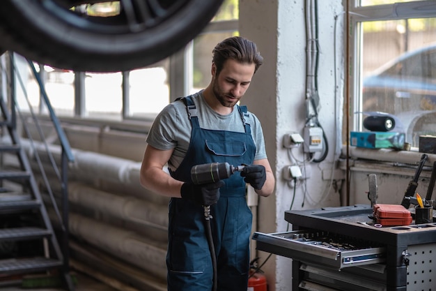 Concentrated young Caucasian auto mechanic in work clothes attaching the nozzle to the impact wrench