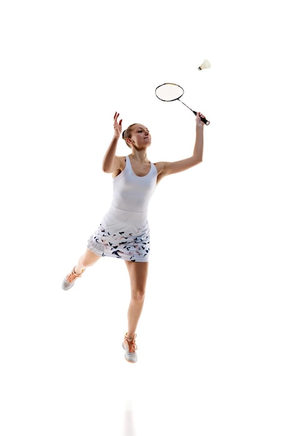 Concentrated young girl athlete in motion with racket playing badminton isolated over white