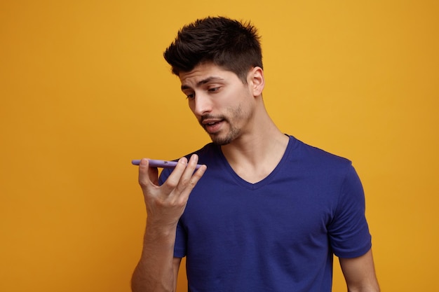 Concentrated young handsome man talking on phone using its microphone on yellow background