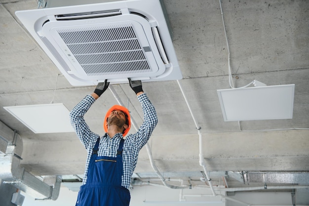 Concentrated young Indian engineer setting up air conditioner