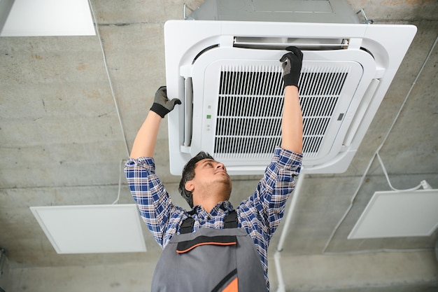 Concentrated young Indian engineer setting up air conditioner