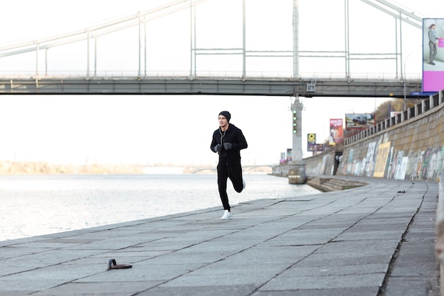 Сосредоточенный молодой человек-спортсмен, бегущий по набережной осенью