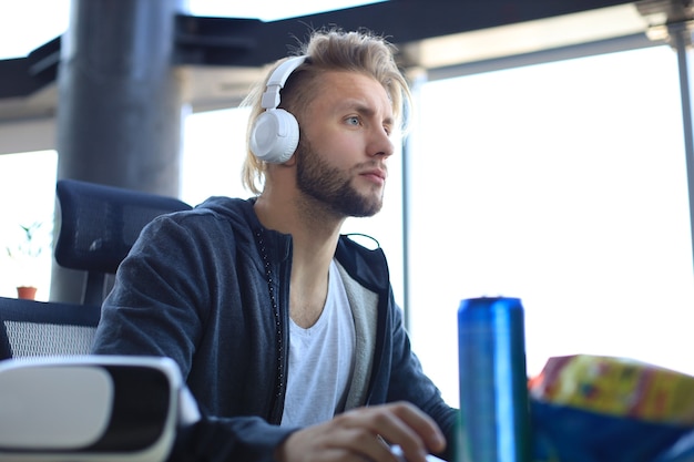 Concentrated young man in casual clothing using computer, streaming playthrough or walkthrough video.