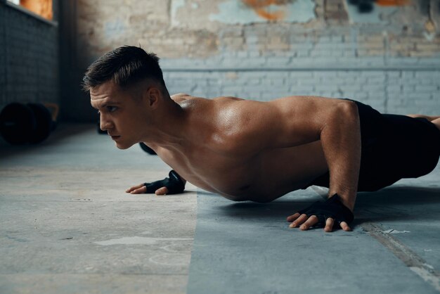 Photo concentrated young man doing pushup exercises in gym