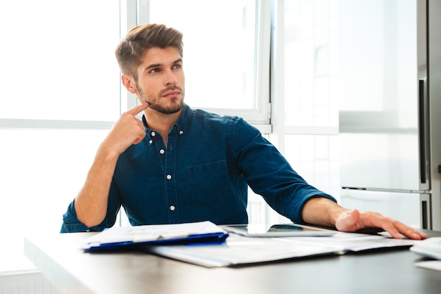 Concentrated young man at home thinking about finances. Look aside and touching his face