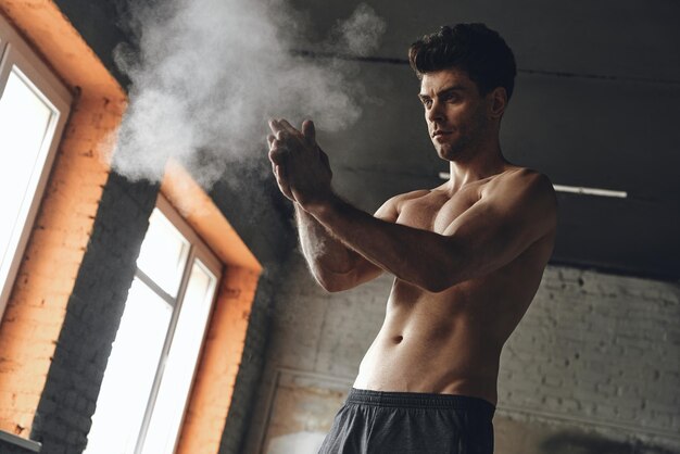 Concentrated young man preparing hands with talcum powder before training