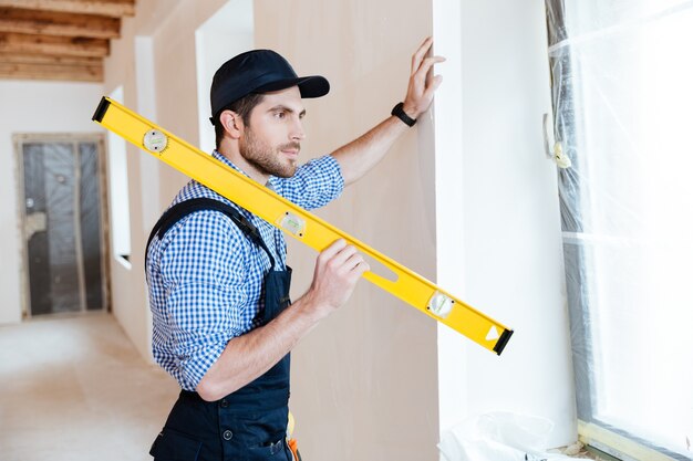 Concentrated young repairman standing with a level in his hands and watching at the window