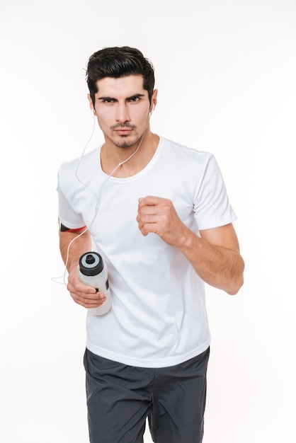 Concentrated young sports man running with earphones and water bottle isolated on a white background