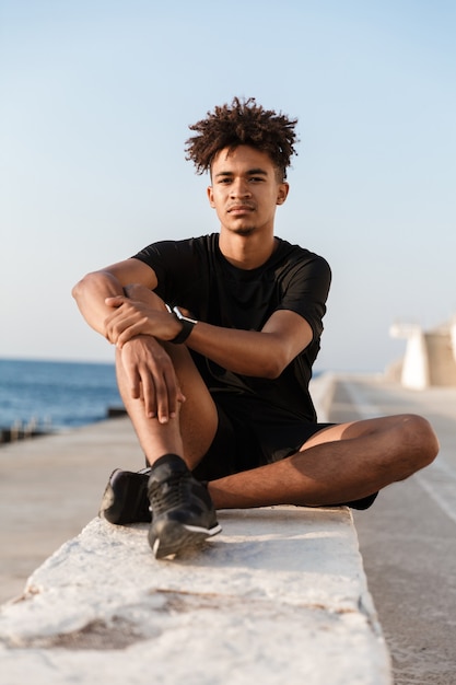 Concentrated young sportsman sitting outdoors on the beach