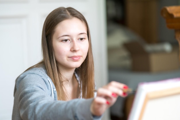 Concentrated young woman painting on canvas