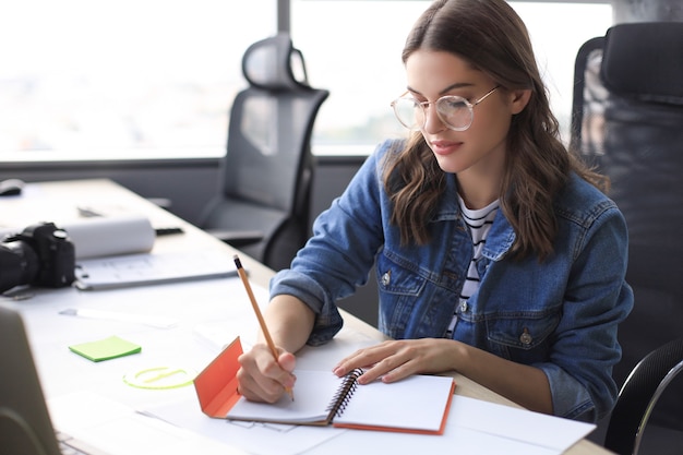 Concentrated young woman writing something down while working in the office.