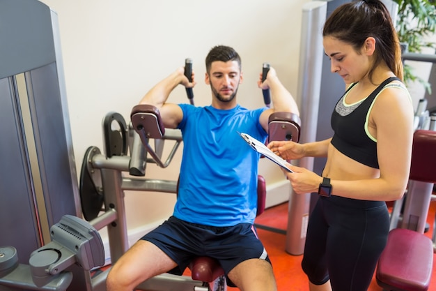 Concentrating man using weights machine with trainer