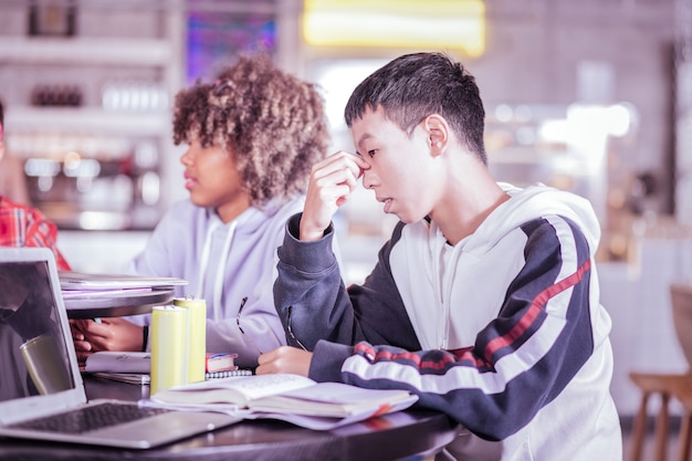 Concentreer je op de taak. Knappe Aziatische jongen zit in halve positie tijdens het denken over onderzoek