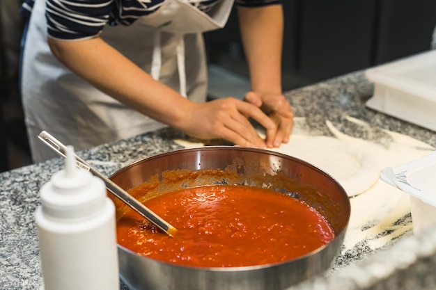Foto concentreer je op de tomatensaus vrouwelijke kok die op de achtergrond werkt en het pizza deeg knett