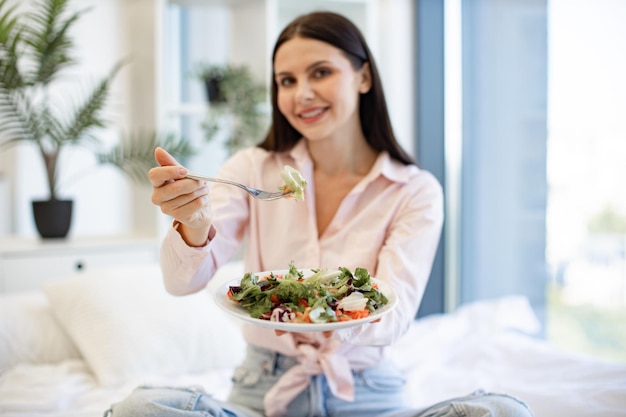 Concentreer je op het bord met salade en vork in de handen van een vrouw die van het ontbijt geniet.