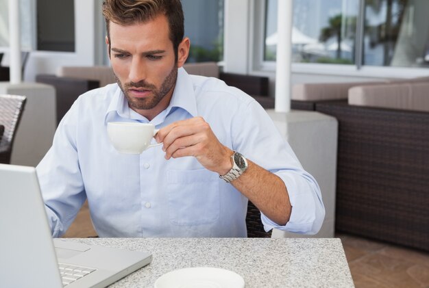 Concentrerende zakenman die met laptop het drinken koffie werkt